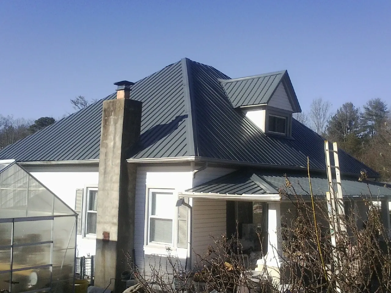 Dark blue standing seam metal roof on a white farmhouse with dormer — Slate & Tile Roof Repair by Roofing Brothers in Lake Saint Louis