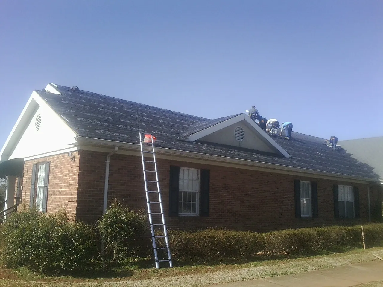 Crew tearing shingles off a brick ranch roof with a ladder set — Metal Roof Repair work by our crew in Lake Saint Louis
