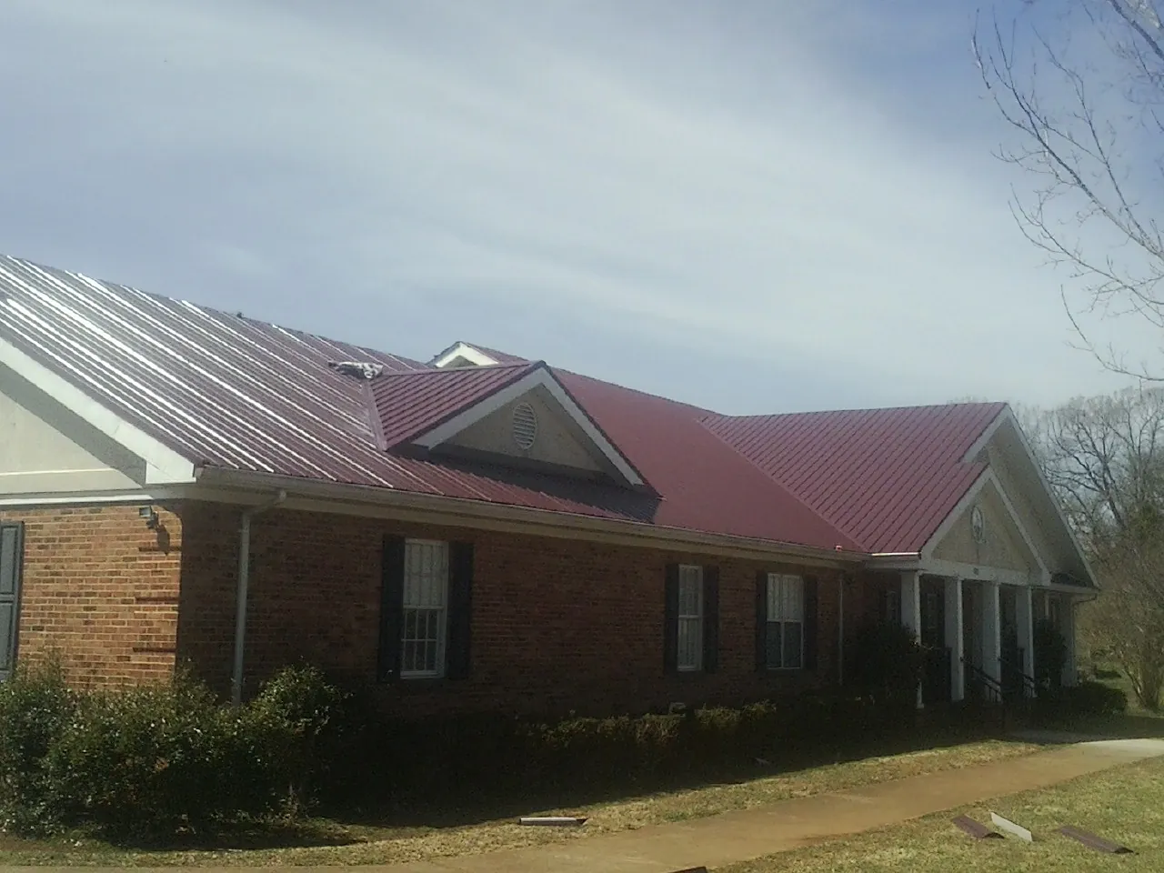 Red metal roof with gabled entries on a long brick building, from a Hail Damage Roof Repair job in Lake Saint Louis