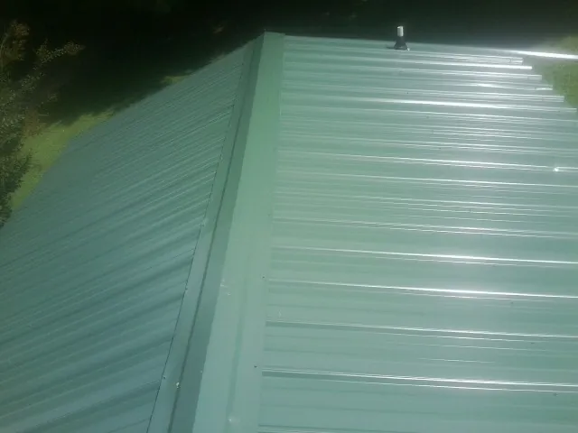 New green metal panels meeting at the ridge of a roof — Flat Roof Repair work by our crew in Lake Saint Louis