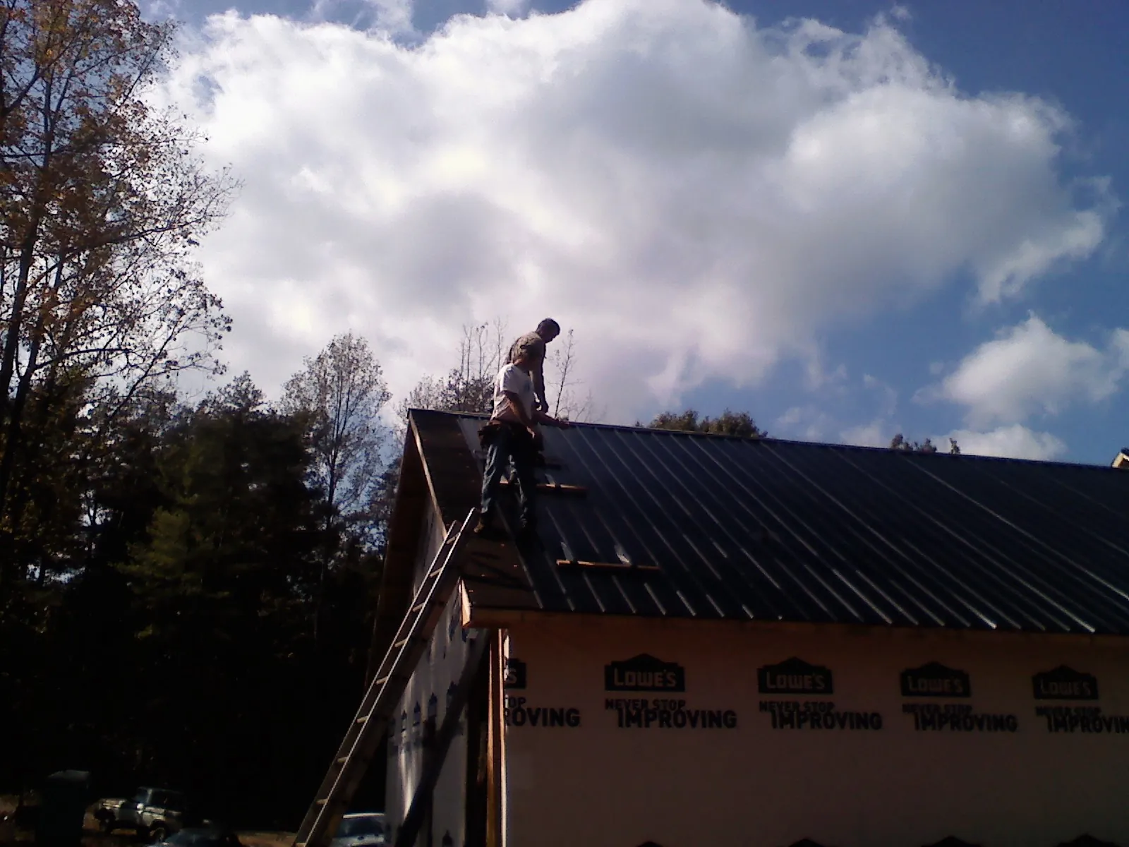 Roofer fastening dark metal panels high against a cloudy sky, from a Roof Inspection job in Lake Saint Louis