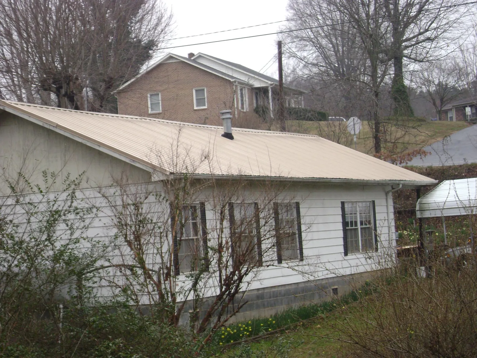 Tan metal roof on a white sided house set into a hillside — Commercial Roofing by Roofing Brothers in Lake Saint Louis