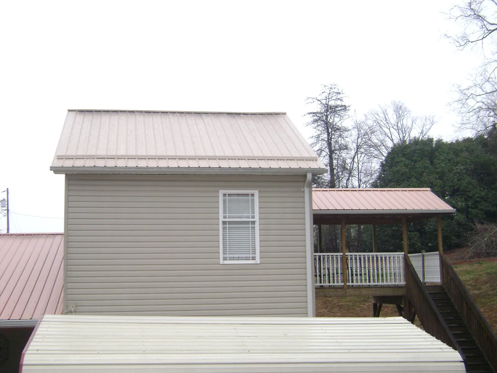 Tan metal roofs on a two story addition and attached porch, from a Roof Replacement job in Lake Saint Louis
